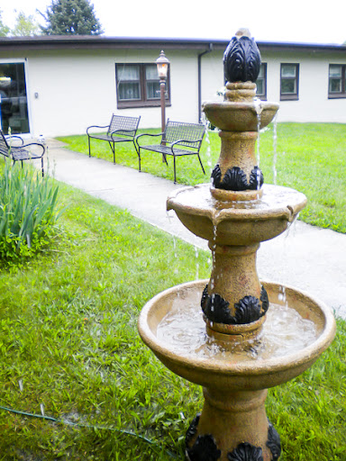 A serene outdoor scene featuring a decorative fountain surrounded by lush green grass and benches.