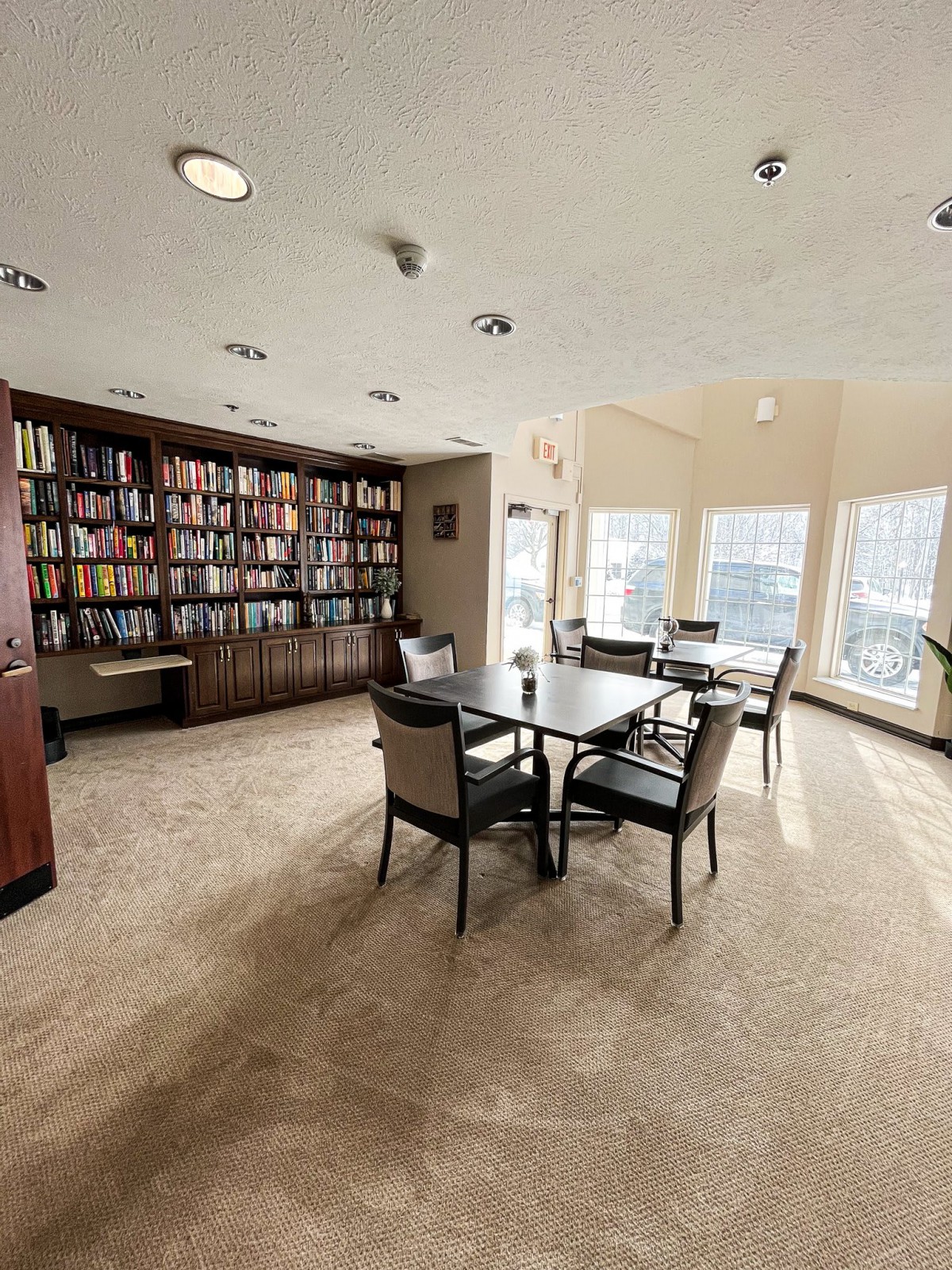 A cozy library with bookshelves, a table, and chairs, bathed in natural light.