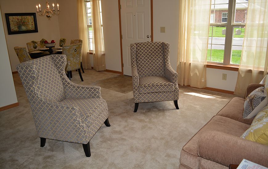 A cozy living room with patterned chairs and large windows adorned with curtains.
