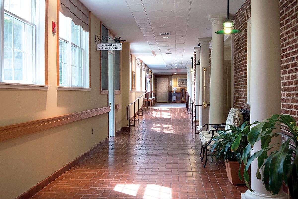 A well-lit interior hallway with brick flooring and seating areas along the side.