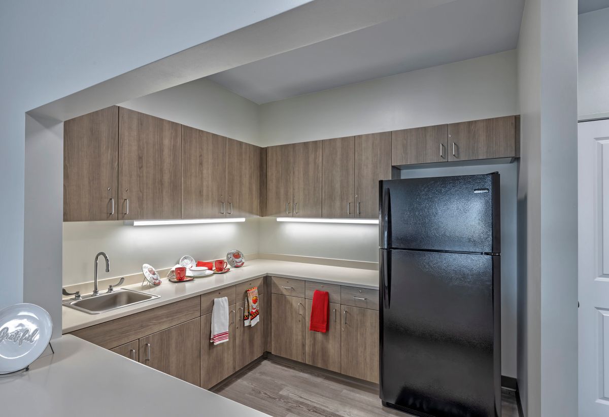 A modern kitchen with wooden cabinets, a black refrigerator, and red accent decorations.