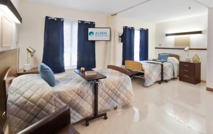 A hospital room with two beds, featuring blue curtains and essential medical furniture.