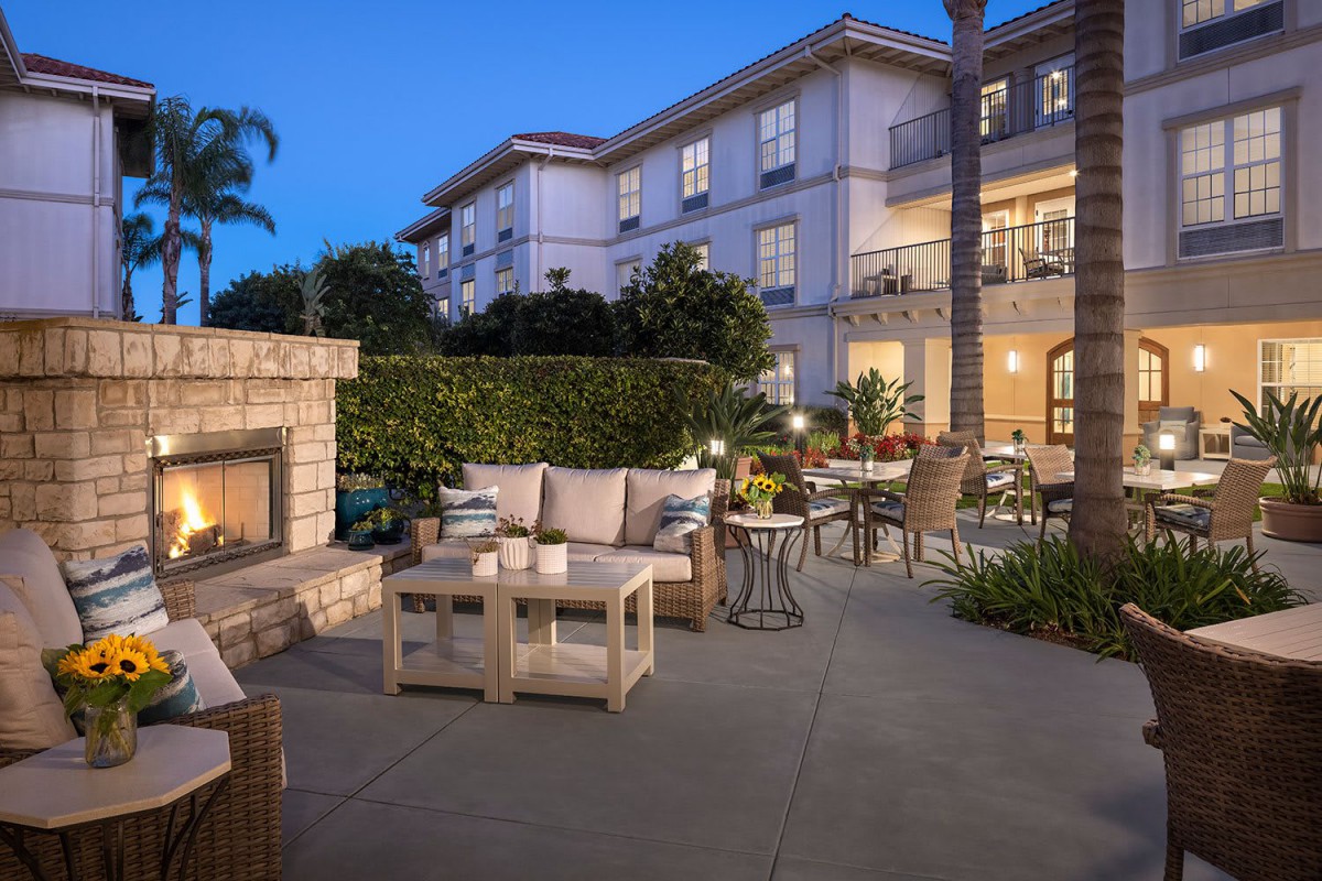 A cozy outdoor patio area with comfortable seating and a fireplace in front of an apartment building during the evening.