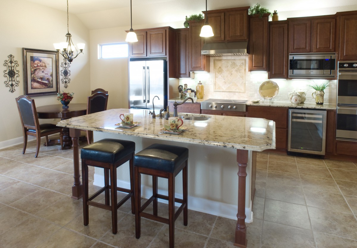 A modern kitchen with a large island and granite countertops, featuring wooden cabinets and pendant lighting.