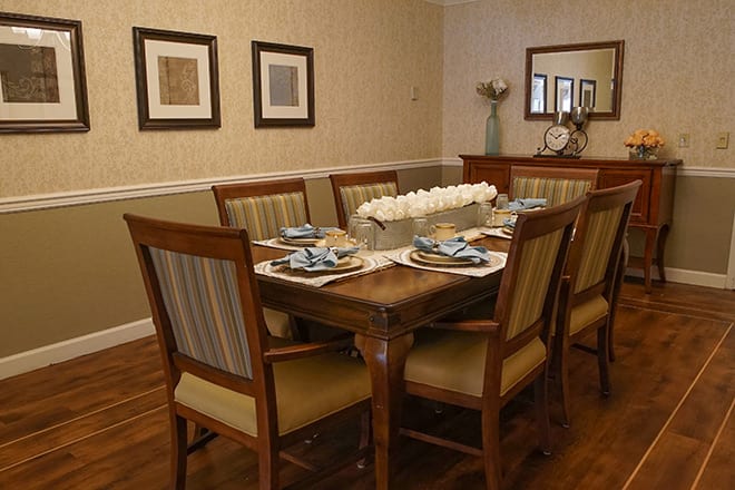 A well-decorated dining room with a large wooden table set for a meal, featuring chairs with striped upholstery and minimalistic wall art.