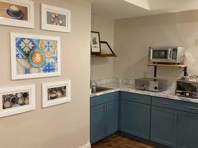 A cozy kitchen corner featuring blue cabinets, wall-mounted artwork, and a compact countertop setup with a microwave.