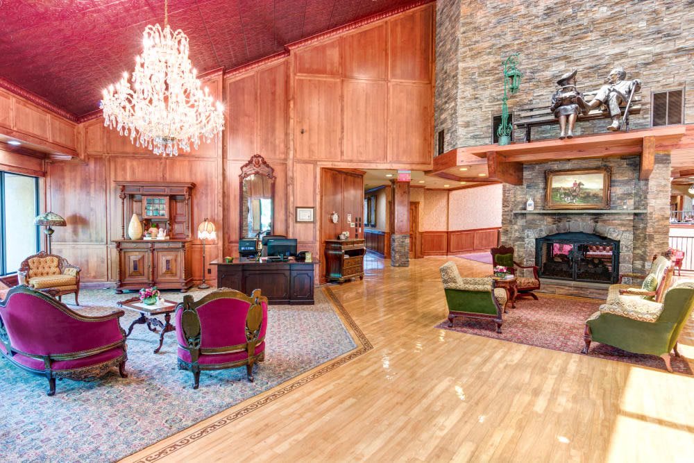 A luxurious living room featuring a grand chandelier, wood paneling, and a stone fireplace with elegant furniture.