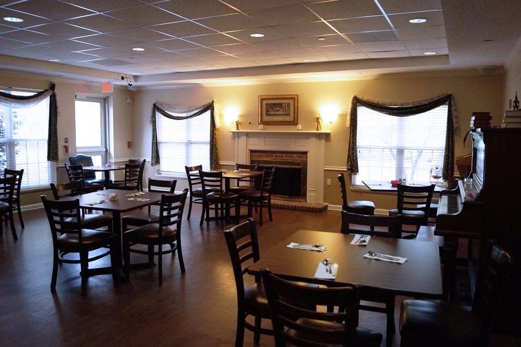 A cozy dining room with neatly arranged tables and chairs, featuring a fireplace and large windows.