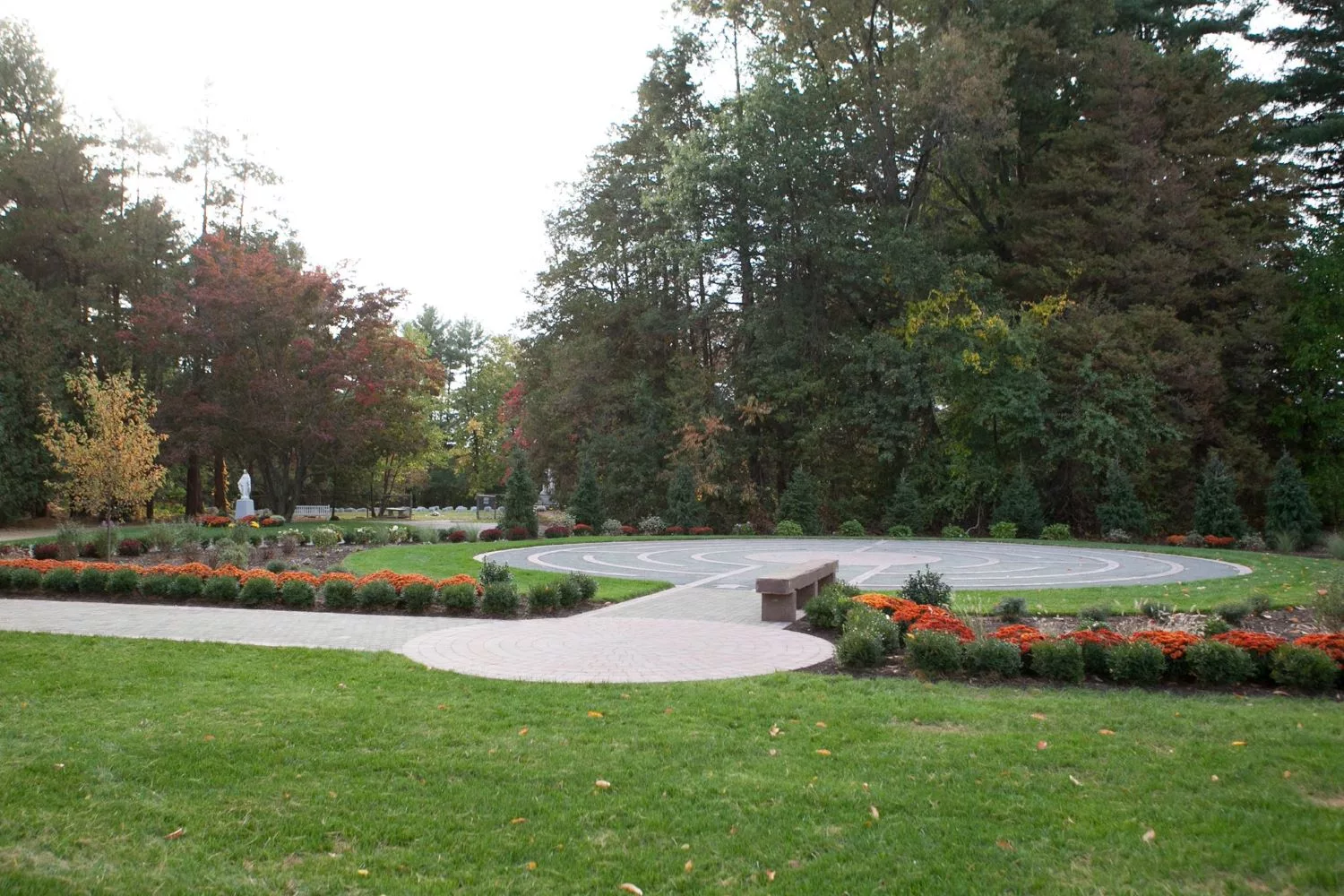 A serene park setting with a pathway surrounded by lush greenery and colorful flowers.
