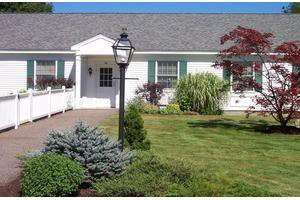 A well-maintained front yard with a white house, surrounded by greenery and featuring a central lamp post.