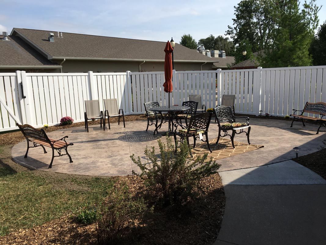 A neatly arranged patio area with outdoor furniture and an umbrella, enclosed by a white fence.
