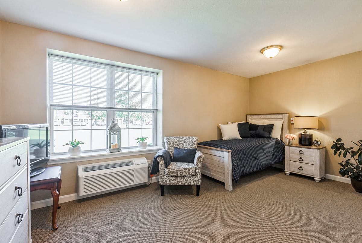A cozy bedroom with neutral colors featuring a bed, armchair, and large window.