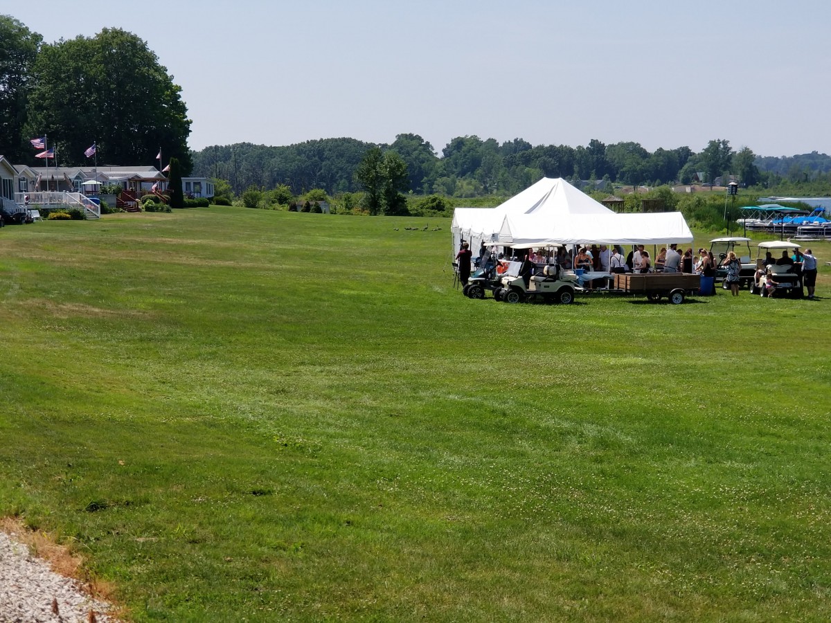 A group of people gathered under a tent in an open field on a sunny day.