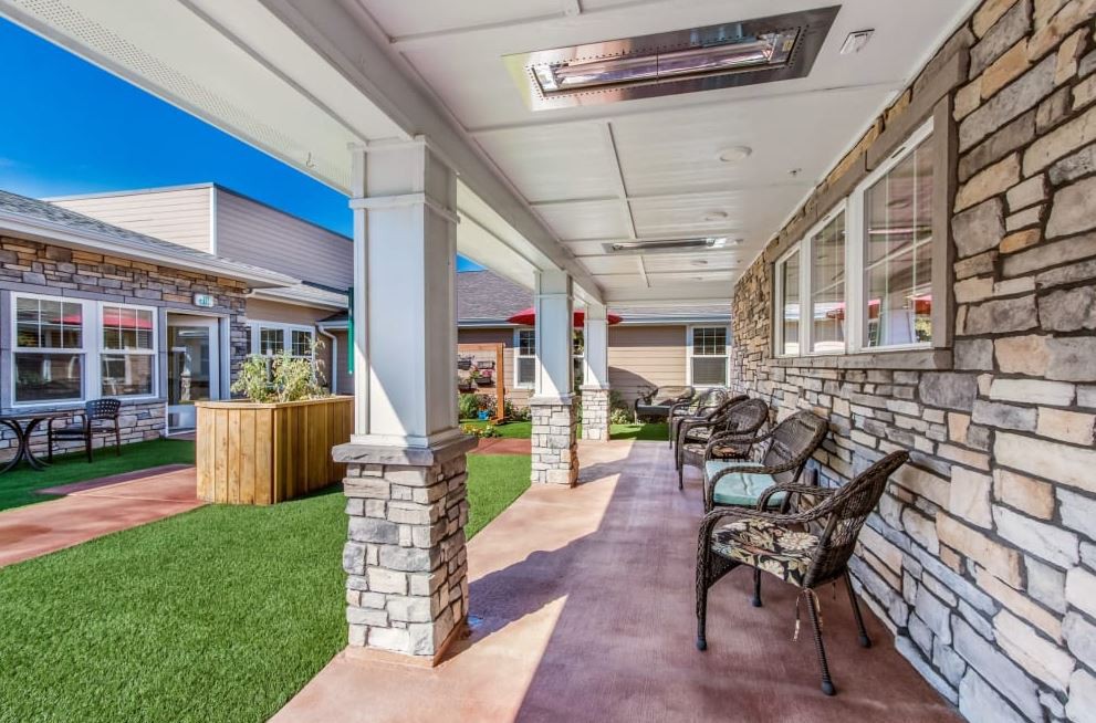 A sunny patio with outdoor seating under a covered porch, featuring stone columns and a well-maintained yard.