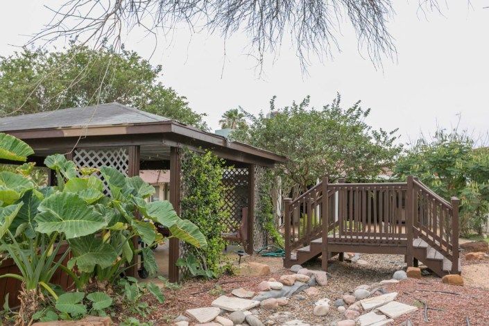 A tranquil garden setting with a wooden gazebo and deck surrounded by lush greenery.