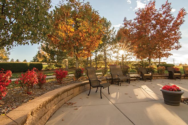 A sunny patio with chairs surrounded by colorful autumn foliage.