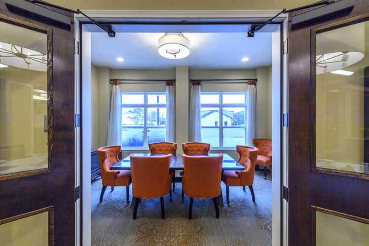 A modern conference room featuring a large table surrounded by orange chairs and bright windows.
