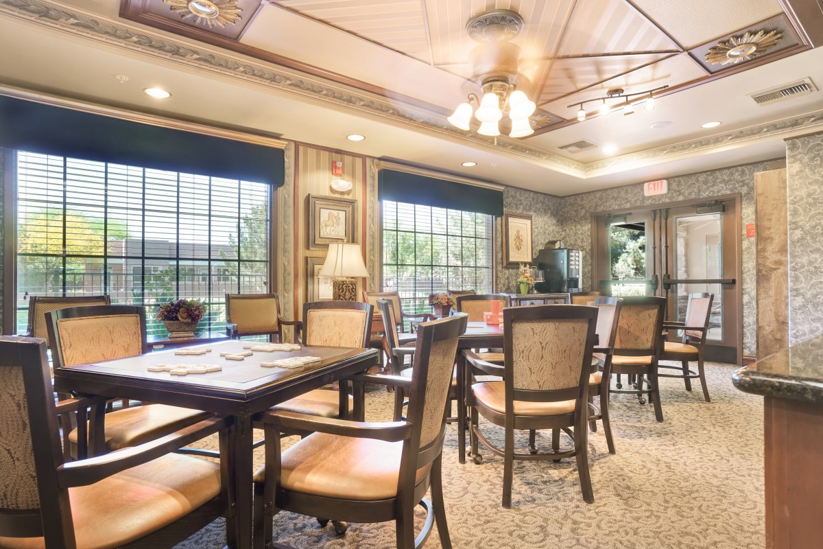 A cozy dining area filled with tables and chairs, illuminated by natural light from large windows.