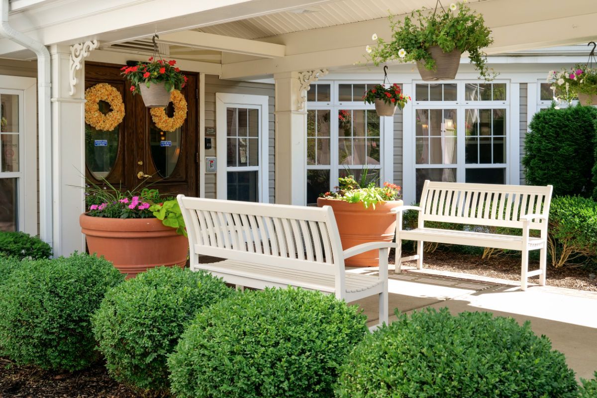A cozy outdoor seating area with white benches surrounded by lush greenery and potted plants.