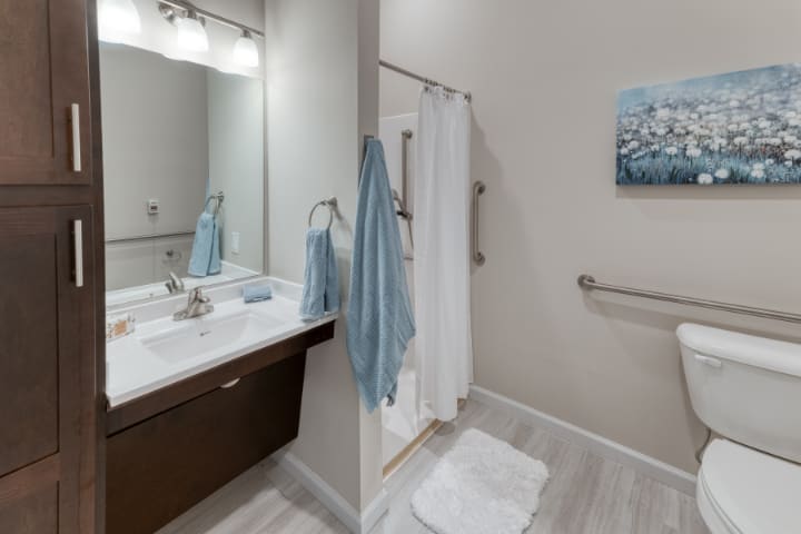 A modern bathroom featuring a sink with a mirror, a shower area with towels, and minimalist decor.
