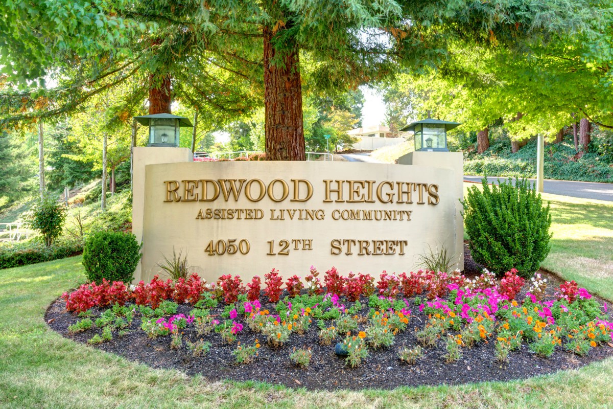 Entrance sign for Redwood Heights Assisted Living Community surrounded by flowers.