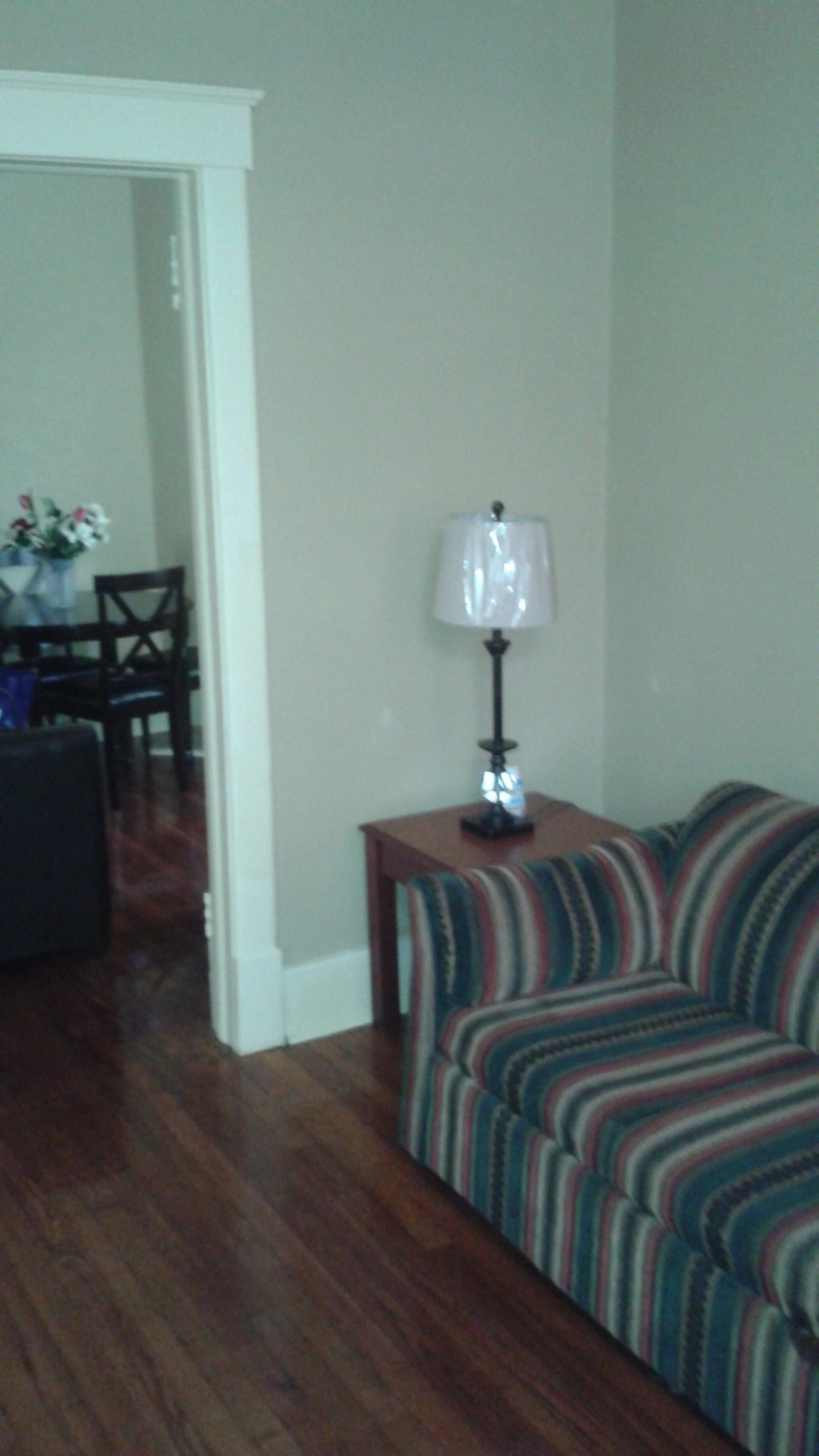 A cozy living room with a striped sofa, side table, and lamp, leading into a dining area.
