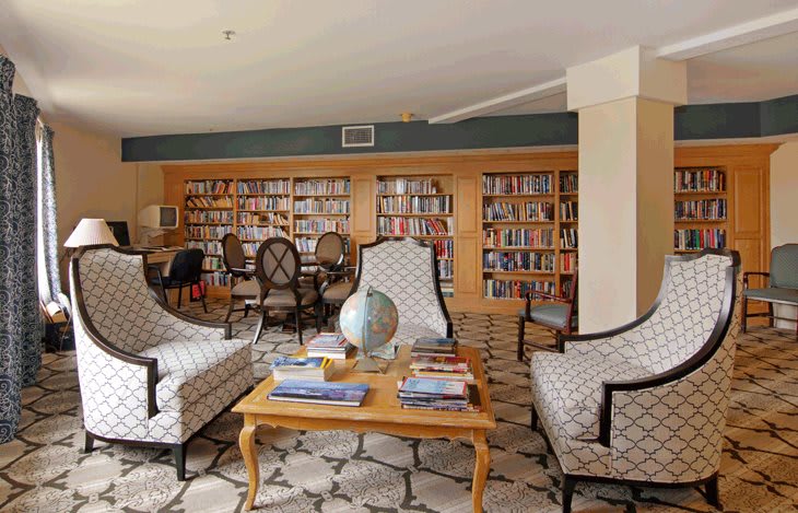 A cozy library with comfortable armchairs, filled bookshelves, and a globe on the coffee table.
