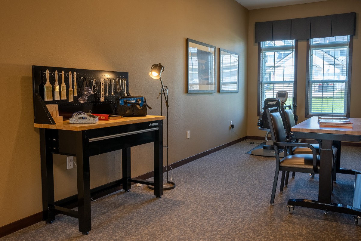 A well-organized workshop space with a desk and tools, featuring a standing lamp and natural light from the window.