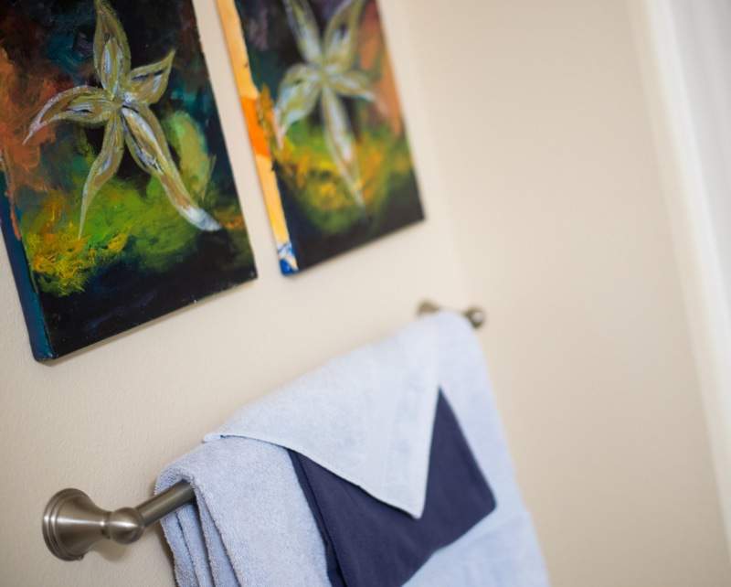 A neatly folded towel hangs beneath vibrant flower-themed artwork in a bathroom.