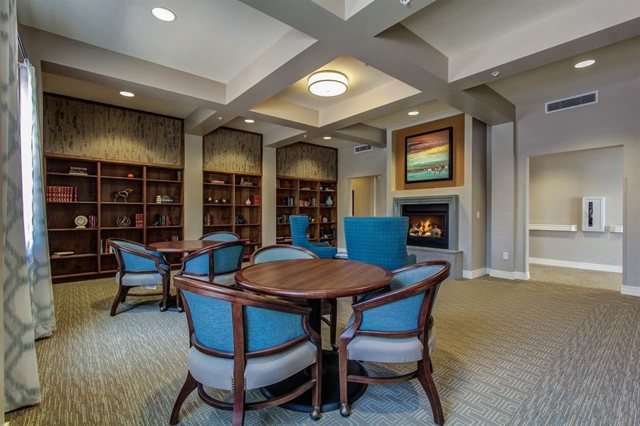 A cozy library interior with comfortable chairs around a table, surrounded by bookshelves and a fireplace.
