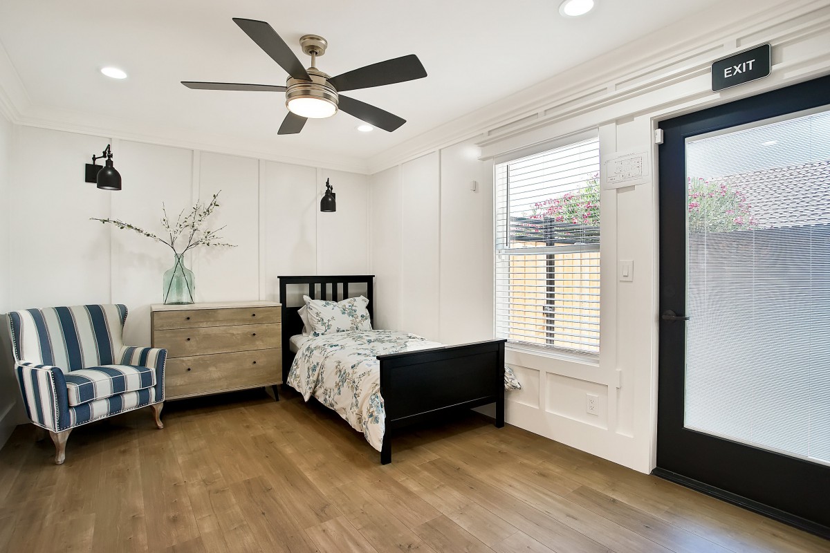 A modern and minimalist bedroom with a single bed, wooden flooring, and ample natural light.