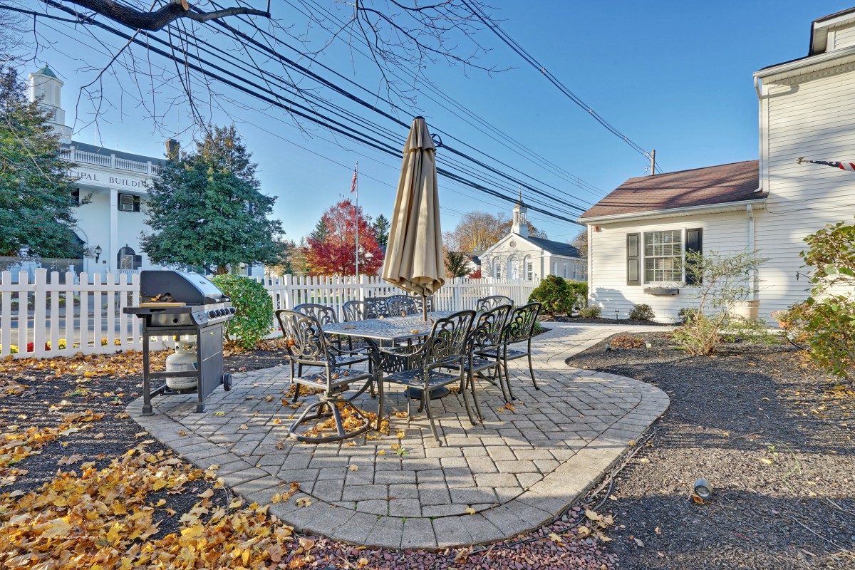 A cozy backyard patio with a table, chairs, and a grill set on brick pavers.