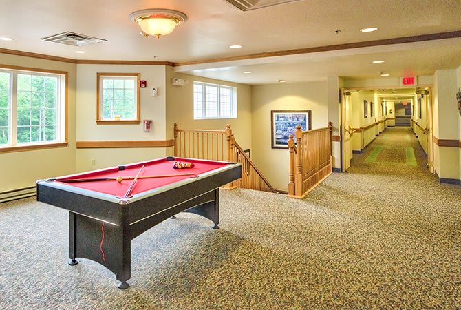 A cozy indoor game room with a pool table in a carpeted hallway featuring natural light from windows.