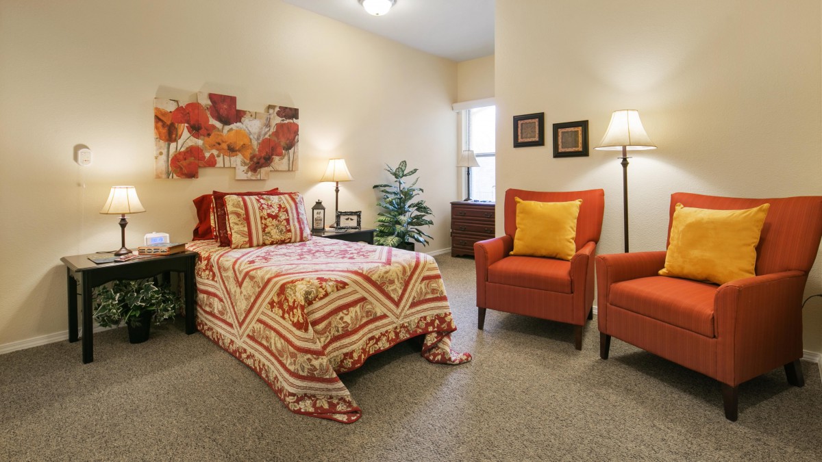 Cozy bedroom with stylish decor, featuring a patterned bedspread, two orange chairs, and warm lighting.