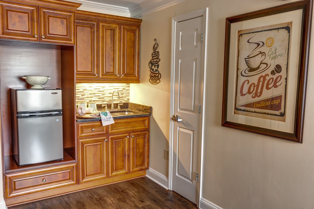 A cozy kitchen nook featuring wooden cabinets, a small fridge, and a coffee-themed poster on the wall.