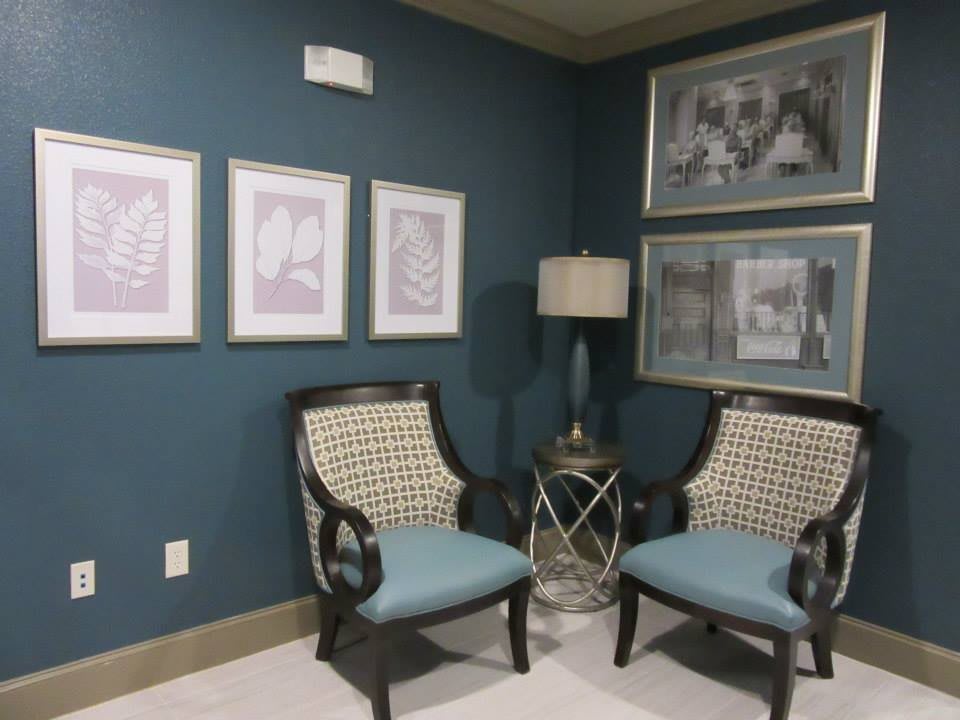 A cozy corner featuring two elegant chairs with blue cushions, a stylish lamp, and framed artwork on the blue walls.