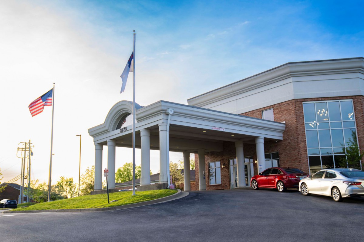 The front entrance of a hotel with a car parked outside and a flag displayed.