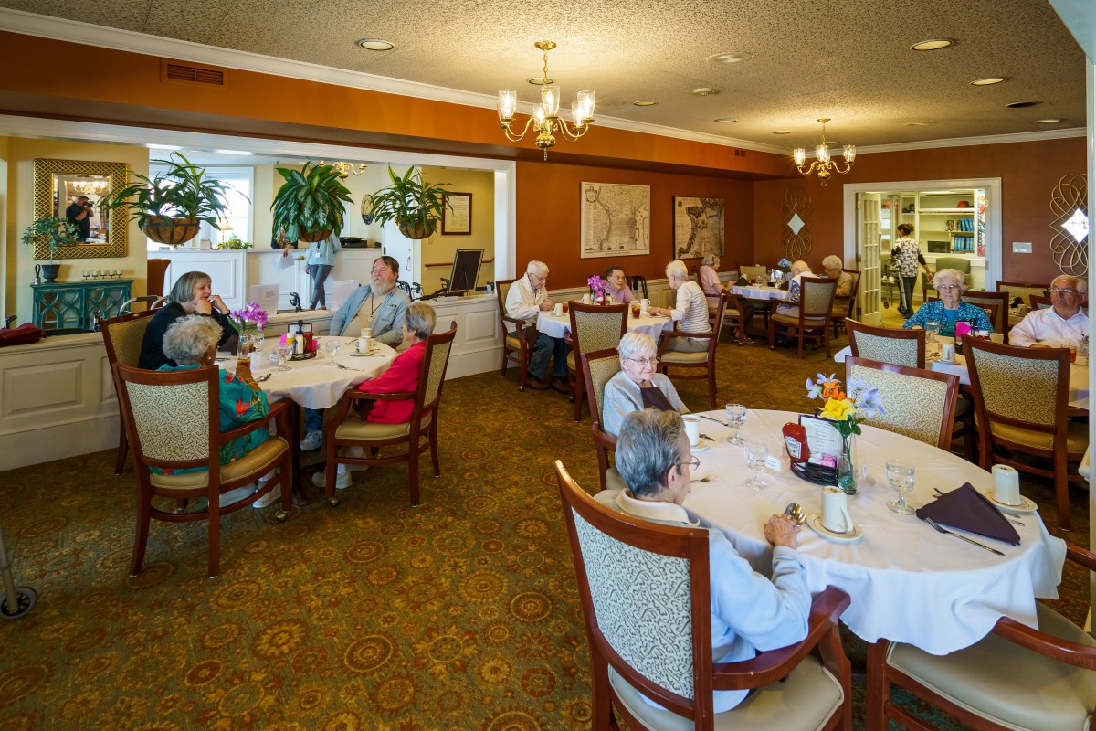 A group of elderly individuals gathered in a dining room, enjoying a meal together at various tables.