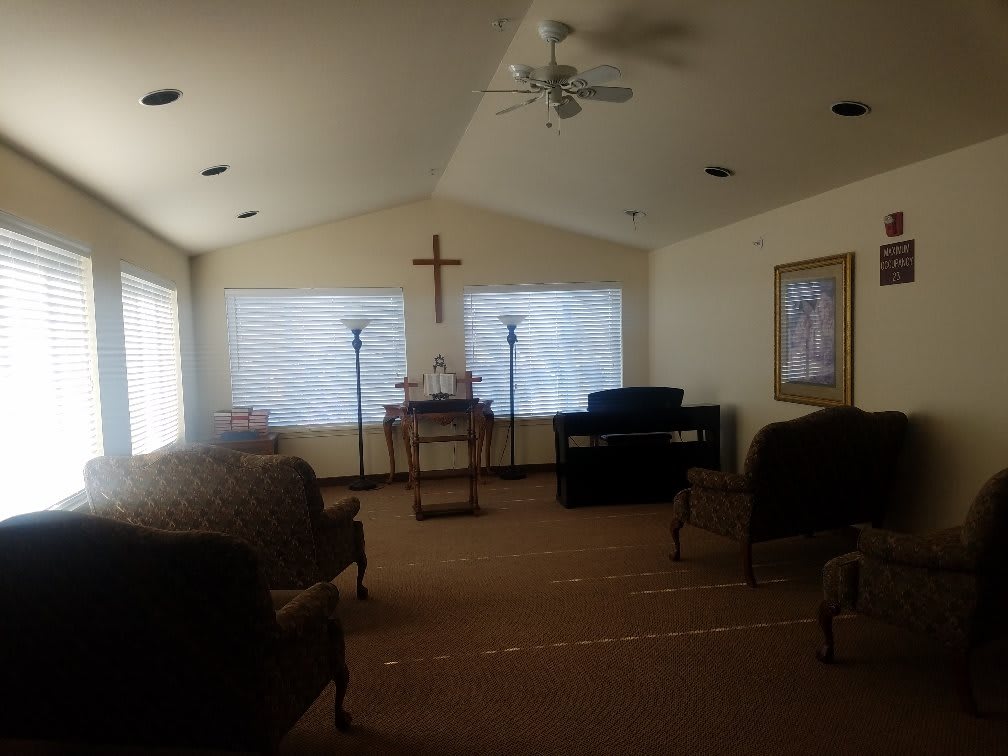 A small chapel interior with a cross on the wall, surrounded by chairs and soft lighting.