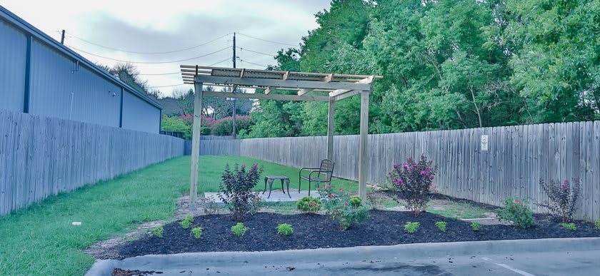 A peaceful garden area with a wooden pergola and neatly arranged plants.
