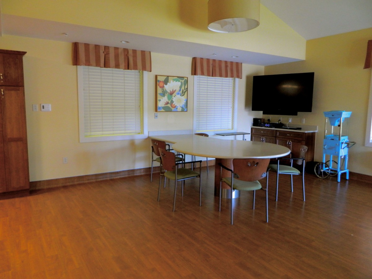 A cozy dining room with a round table and chairs, featuring a television and wooden flooring.