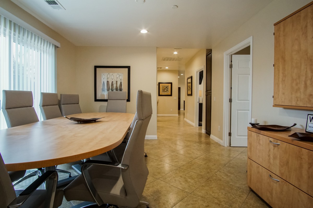 A well-lit conference room with a large meeting table and chairs, featuring artwork on the walls and an adjoining hallway.