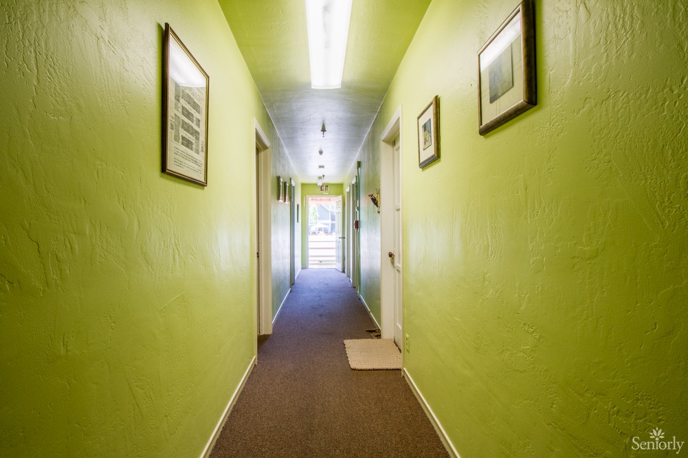 A long hallway with green walls, several doors, and framed pictures along the corridor.