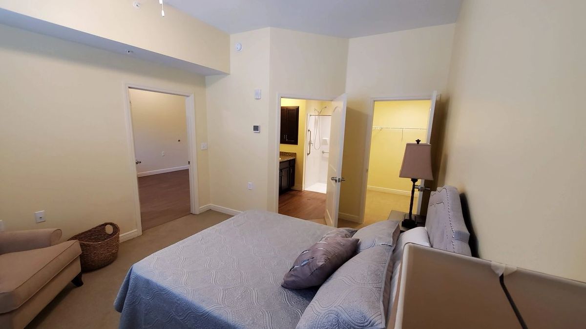 A cozy bedroom with a neatly made bed, neutral color palette, and multiple doorways leading to adjoining rooms.