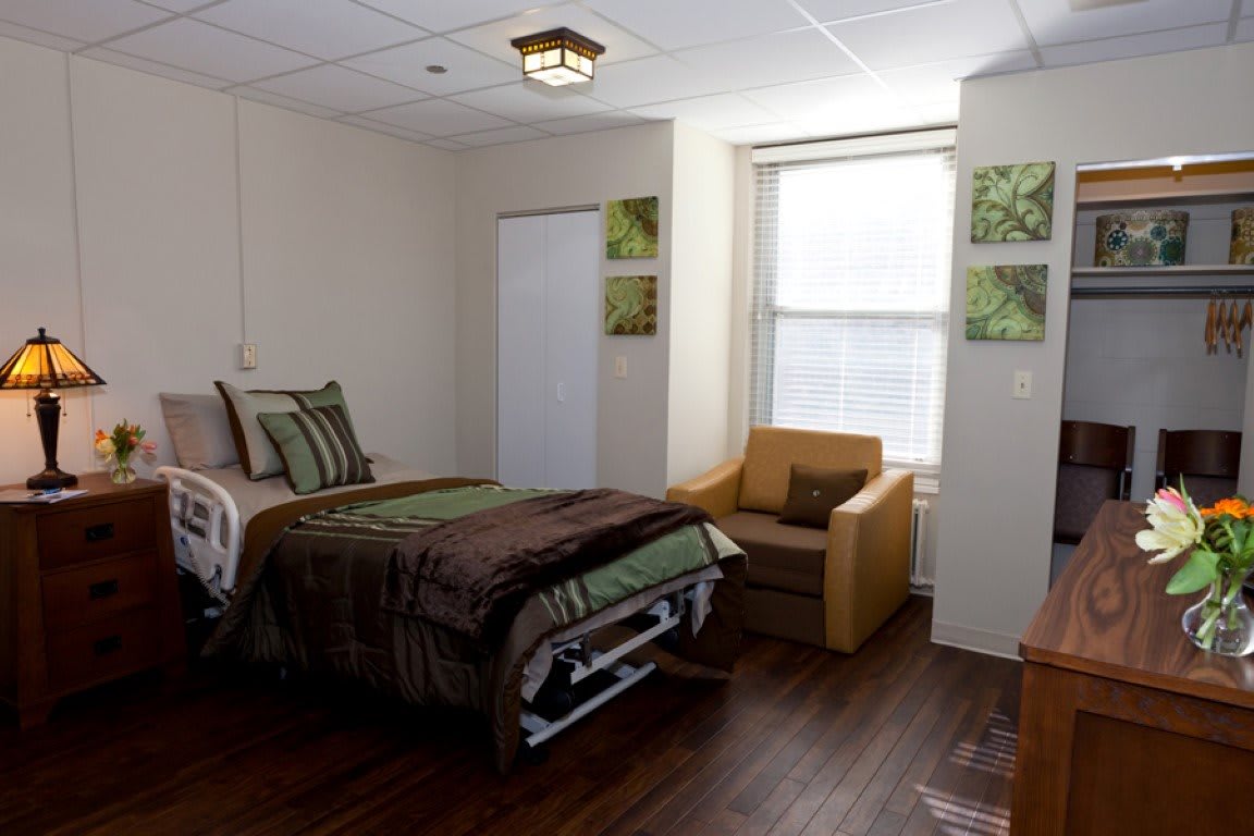 A well-arranged hospital room with a single bed and a comfortable chair near the window.