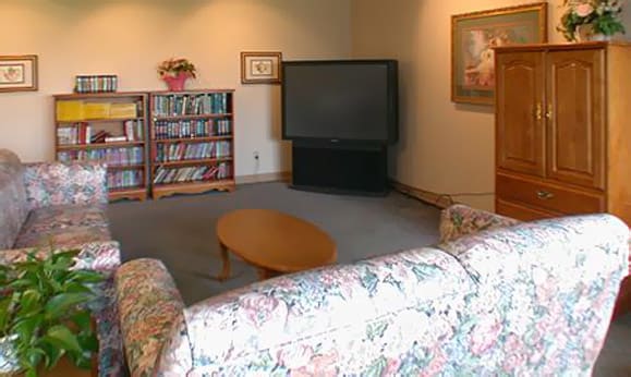 A cozy living room with a large television, bookshelf, floral sofa, and wooden coffee table.