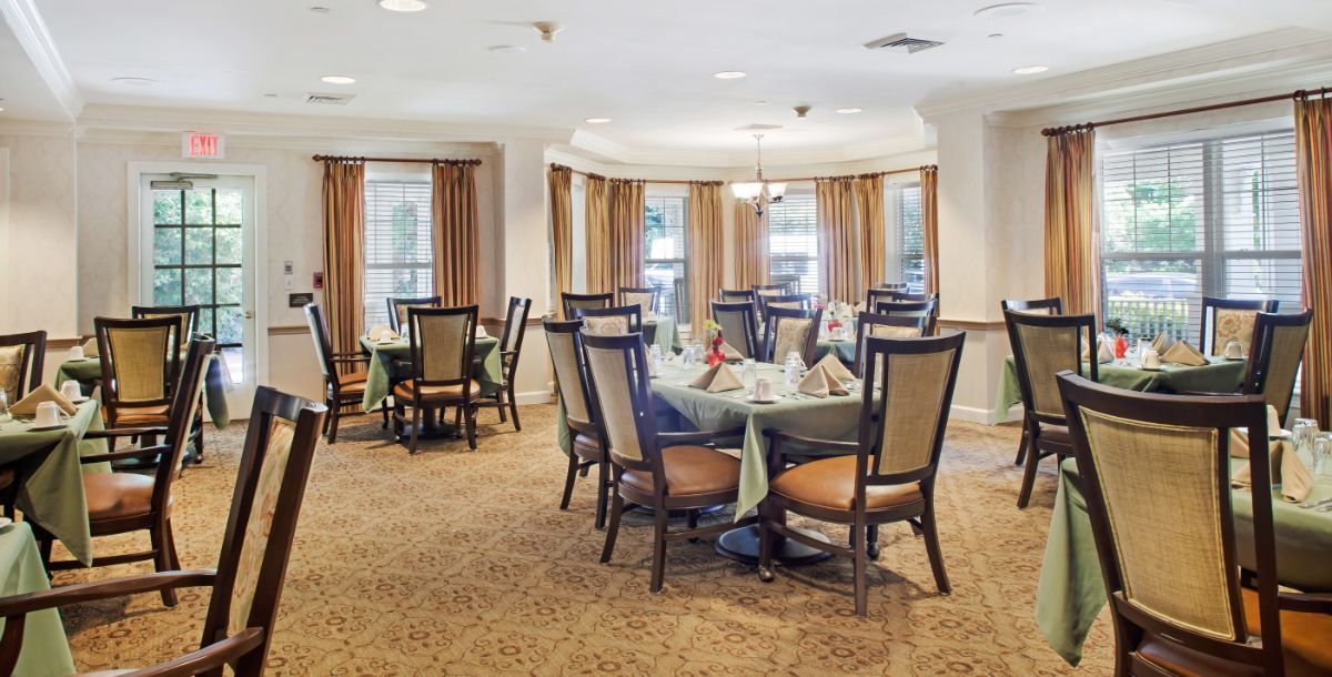 A well-decorated dining room with multiple tables and chairs, featuring warm lighting and carpeted flooring.