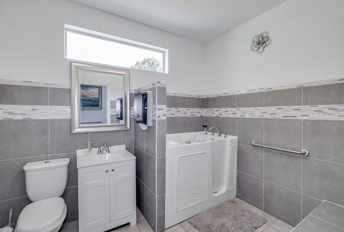 A modern bathroom featuring a walk-in tub, sink with mirror, and tiled flooring.