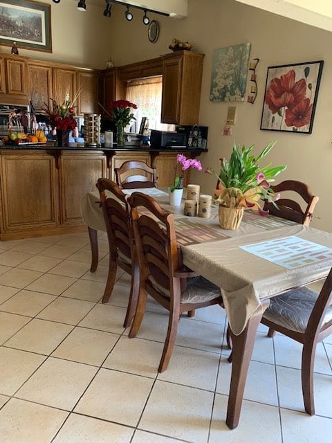 A cozy kitchen and dining area with a wooden table and chairs, adorned with plants and flowers.