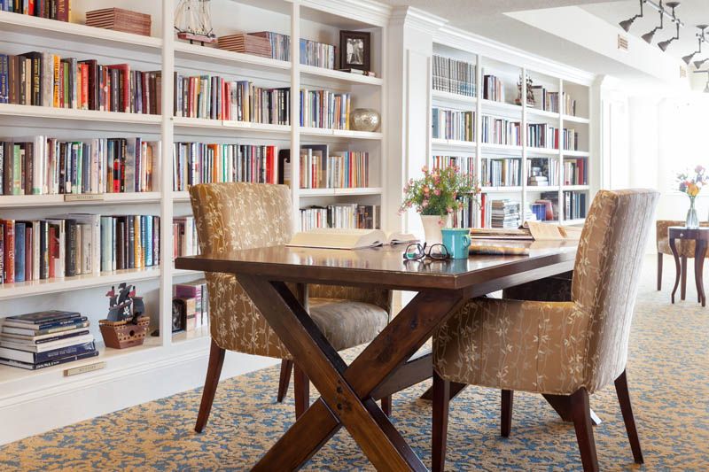 A cozy home library with bookshelves, a wooden table, and comfortable chairs.